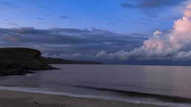 Evening time lapse of the waves crashing over a sandy beach. Clouds roll in the wind in the distance over the cliffs. Filmed on the Isle of Lewis, part of the Outer Hebrides of Scotland.