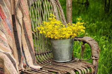 A bucket of wild flowers on an old wicker sofa in the garden. Vintage village photo. Summer on the farm.