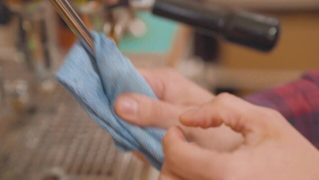 Barista cleans steam wand of coffee machine with cloth and steam. Closeup