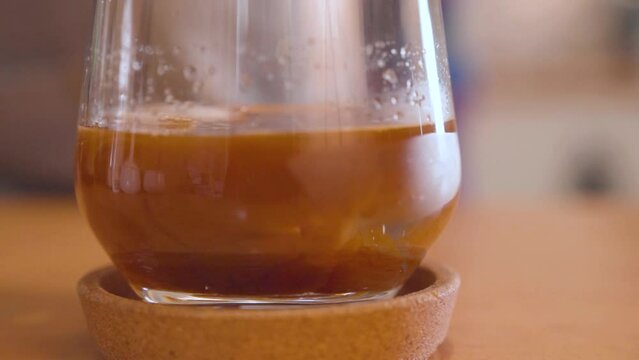 Pouring espresso over melted ice cubes in glass. Handheld closeup