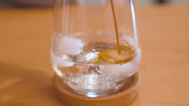 Iced coffee preparation. Pouring espresso over ice cubes in glass. Closeup