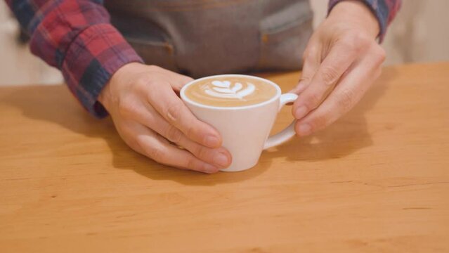Barista puts down to counter cup of cappuccino with latte art. Closeup