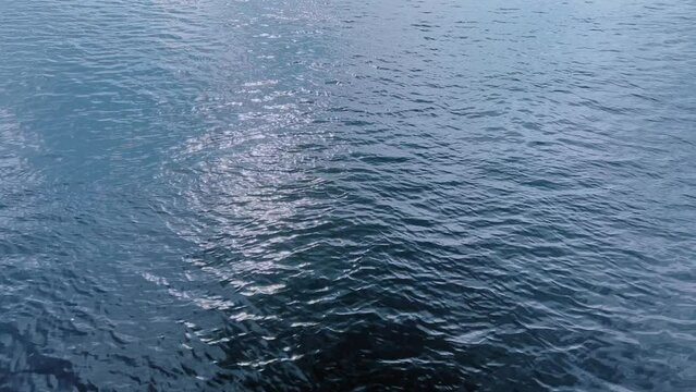 The blue texture of a calm water surface in which sun glare is reflected.