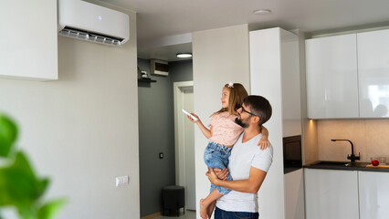 Father with little daughter on hands turn on air conditioner using remote control. Happy family...