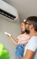 Happy family, father and little daughter fun turn on air conditioner using remote control.