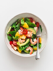 Delicious avocado, mango, shrimp, tomato salad  on a ligth background, top view