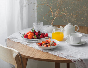 Cozy breakfast served - porridge oatmeal with seasonal fruits and berries, orange juice, tea on a wooden round table