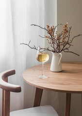 A glass of white wine, autumn decor on a wooden round table in a cozy living room