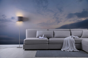 Beautiful sky with clouds as wallpaper pattern. Living room interior with comfortable sofa near wall