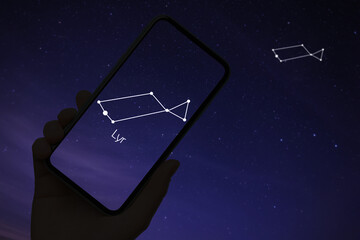 Woman using stargazing app on her phone at night, closeup. Identified stick figure pattern of Lyra constellation on device screen © New Africa