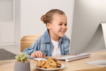 Little girl using computer at table in room. Internet addiction