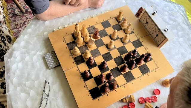 Top view of two aged men playing chess game on white table in the garden at daytime. Retirement life, active seniors concept. quality 4k footage