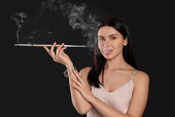 Obraz premium Woman using long cigarette holder for smoking on black background