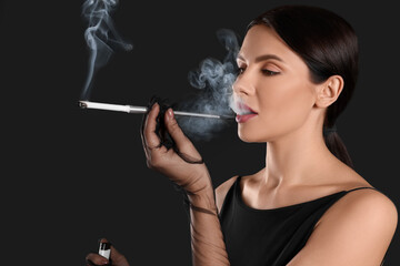 Fototapeta premium Woman using long cigarette holder for smoking on black background