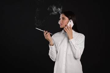 Woman using long cigarette holder for smoking while talking on phone against black background, space for text