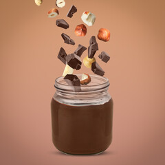 Making yummy chocolate paste. Hazelnuts and pieces of chocolate falling into jar on light brown background