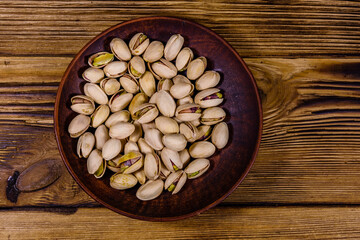Ceramic plate with pistachio nuts on a wooden table. Top view
