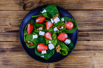 Salad with spinach leaves, feta cheese, walnuts and strawberry on a black plate. Top view