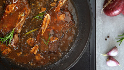 Top view of steak beef ribs in sizzling sauce fry in hot pan on stove. Cooking pieces meat on bone. Food concept