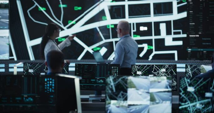 High-Tech Surveillance Office with Multiethnic Specialists Using Satellite Technology to Track a Target Vehicle in Urban Terrain. Large Display Shows Real-Time Monitoring, CCTV Feed and Reports