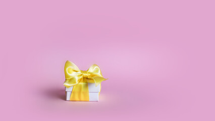 White gift box decorated with yellow satin ribbon bows over pink background, horizontal composition. Christmas or birthday boxing concept