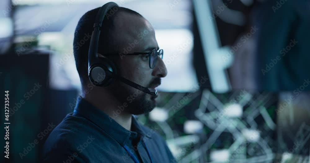 Poster portrait of a surveillance officer wearing a headset, working in a central office hub for cybersecur