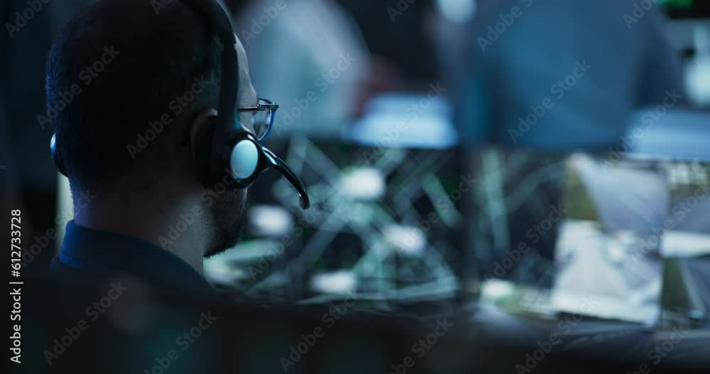 Aufkleber Technical Customer Support Specialist is Talking on a Headset while Working on a Computer in a Call Center Control Room Filled Display Screens and Data Servers. Footage from the Back