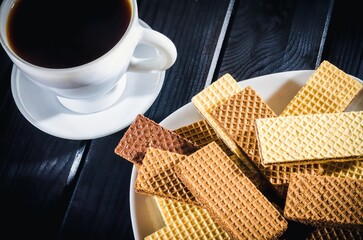 Coffee in a cup with cookies on a plate in the background. Coffee with waffles on a black wooden table. - 612737716