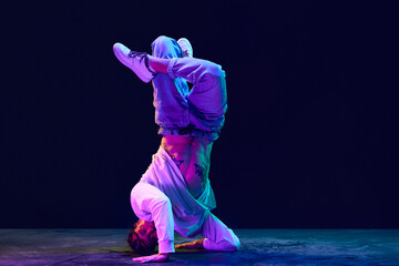 Artistic, sportive young man in sprotive clothes dancing breakdance, hip-hop against black studio...