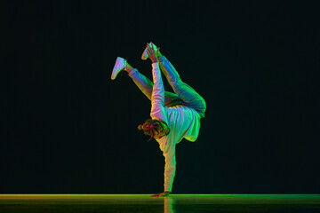 Young artistic guy with dreads, in sport style clothes dancing breakdance, hip-hop against black...