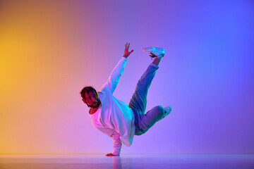 Dance show. Young guy dancing contemp, breakdance and hip-hop against gradient multicolored studio background in neon light