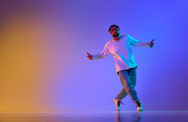 Fototapeta na wymiar Dance show. Young guy dancing contemp, breakdance and hip-hop against gradient multicolored studio background in neon light