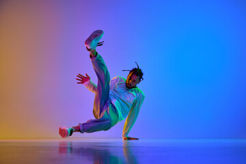 Young guy with dreads, in casual clothes dancing hip-hop, breakdance against gradient multicolored...