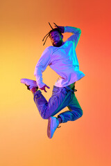 Young bearded man with dreads in casual clothes dancing breakdance against gradient orange yellow...
