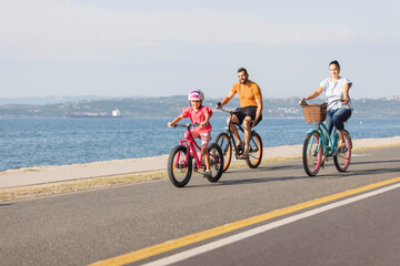 Fototapeta premium Mother, father and girl child having fun on vacation cycling near the sea. Family coastal bike ride.