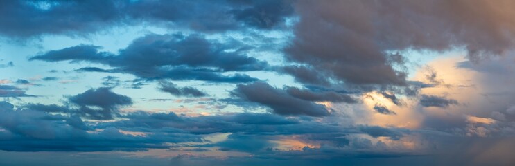 Deep indigo storm clouds hang against the horizon in the rays of the setting sun. - obrazy, fototapety, plakaty