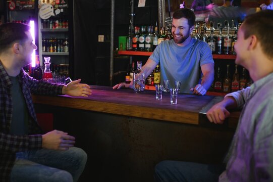Attractive bartender is smiling and taking order of two men sitting at bar counter in pub