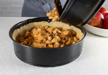 Filling a raw pie in a baking pan with cooked apples for making a apple pie.