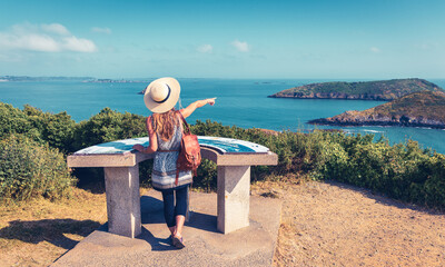 Woman looking at Brittany coast panoramic view,  orientation table- France - obrazy, fototapety, plakaty