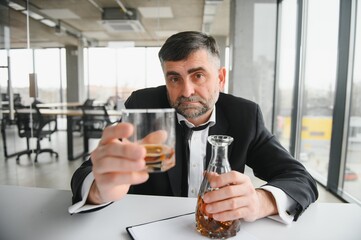Old business man is drinking alchool at the office