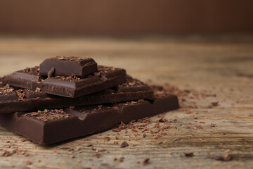 Pieces and shavings of tasty chocolate on wooden table, closeup. Space for text