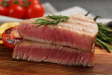 Pieces of delicious tuna steak with rosemary on wooden board, closeup