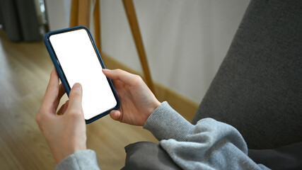 Closeup view of woman hands holding smartphone, lying on couch at home. White screen for advertising text