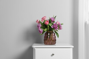 Beautiful bouquet of colorful tulip flowers on white bedside table near white wall