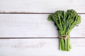 Fresh raw broccolini on white wooden table, top view and space for text. Healthy food