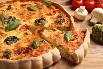 Delicious homemade vegetable quiche and ingredients on wooden table, closeup