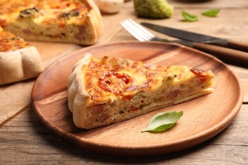 Piece of delicious homemade vegetable quiche on wooden plate, closeup