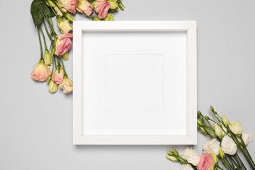 Empty photo frame and beautiful flowers on light gray background, flat lay. Mockup for design