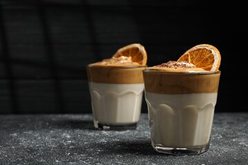 Glasses of delicious dalgona coffee with dry orange and chocolate on grey textured table, space for text