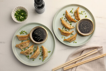 Delicious gyoza (asian dumplings) with soy sauce, green onions and chopsticks on white table, flat lay
